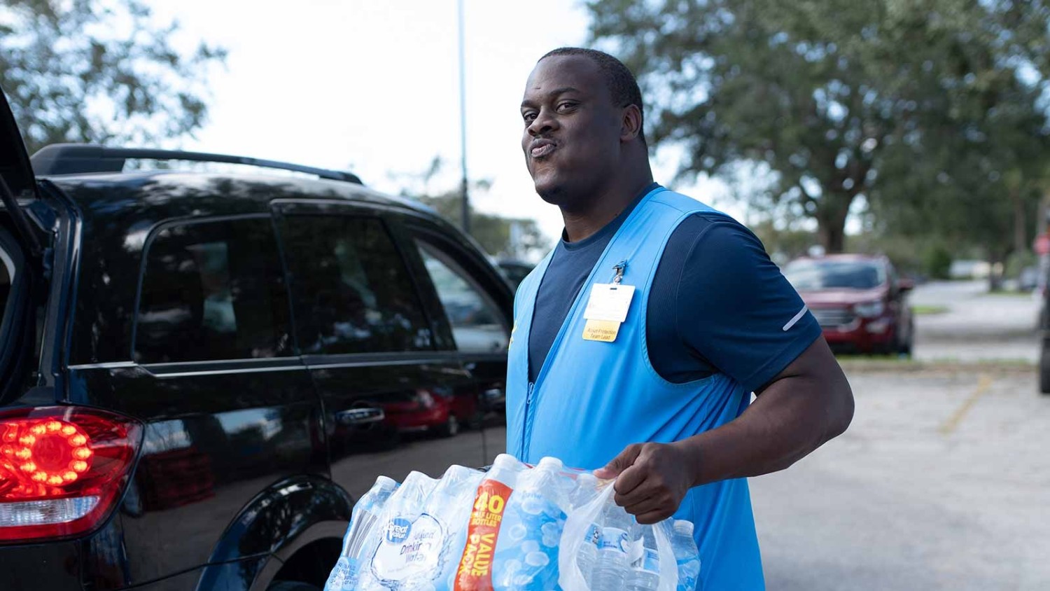 An associate carries a case of bottled water to a customer's trunk.