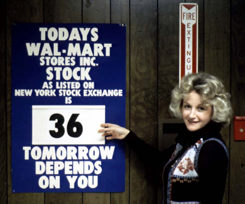 A Walmart associate stands near a New York Stock Exchange sign.