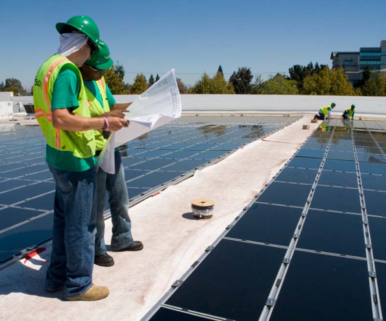 Two workers look at plans during the installment of solar panels.