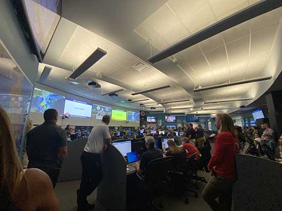 Large room full of people looking at big screens with information about the storm