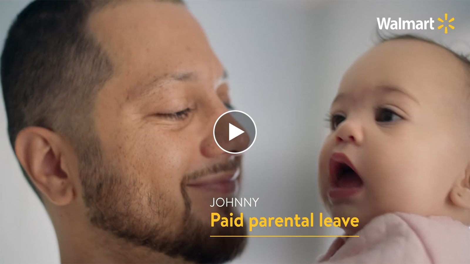 Screen capture with play icon from video. Capture shows man holding baby. Text on screen reads Johnny paid paternal leave.
